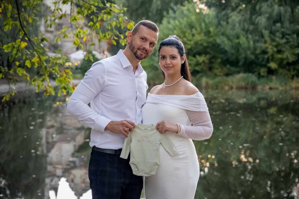 Kismama fotózás 5 Kismama a Párjával egy bodyt tartanak a kezükben.